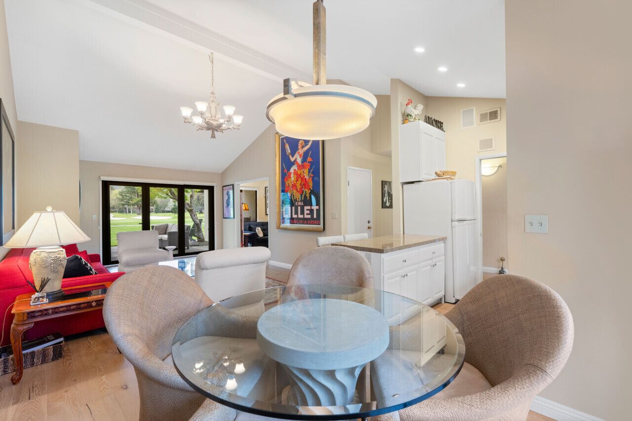 A modern kitchen with a glass dining table, white cabinets, and a chandelier.