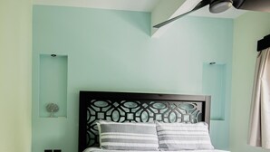 A neatly made bed with a striped bedspread and two pillows, a decorative wall panel, and a ceiling fan. - Palo Rosa 1 (Quepos)