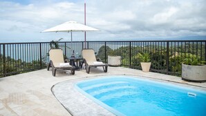 A pool area with two lounge chairs and an umbrella, surrounded by a black metal fence, overlooking a scenic landscape. - Palo Rosa 1 (Quepos)