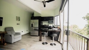 A modern kitchen with a built-in island, a grey sofa, and a ceiling fan. - Palo Rosa 1 (Quepos)