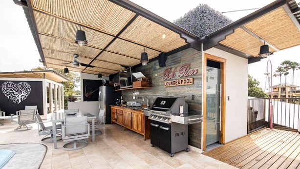 An outdoor kitchen area with a grill, bar stools, and a poolside seating area. - Palo Rosa 1 (Quepos)