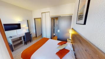 A hotel room with a bed, desk, chair, TV, and a door leading to a bathroom.
