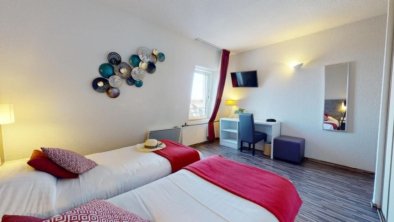 Habitación de hotel con dos camas, un escritorio, una silla, un televisor y un espejo.