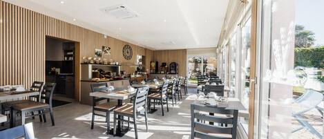 A modern restaurant with a long dining area, wooden paneling on one wall, and large windows.