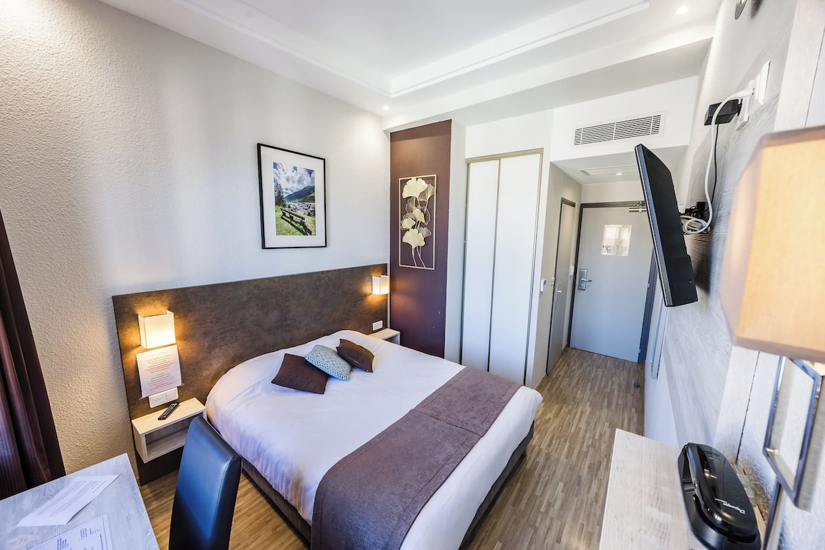 A hotel room with a bed, bedside tables, a TV, a framed picture on the wall, and a door leading to another room.