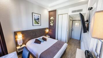 A hotel room with a bed, bedside tables, a TV, a framed picture on the wall, and a door leading to another room.