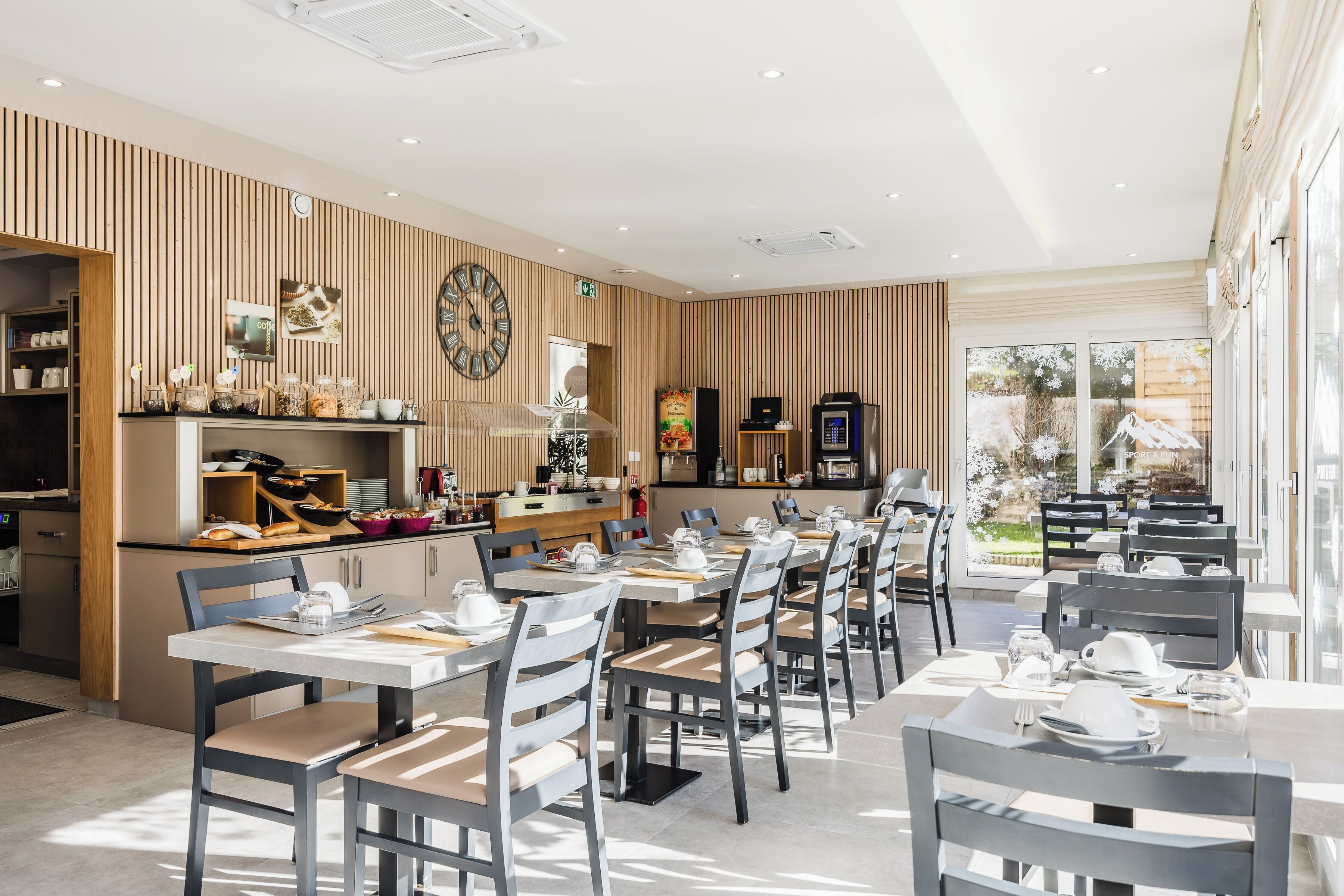 A modern restaurant with wooden panel walls, a kitchen area, and tables set for dining.