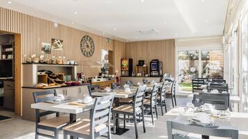 A modern restaurant with wooden panel walls, a kitchen area, and tables set for dining.