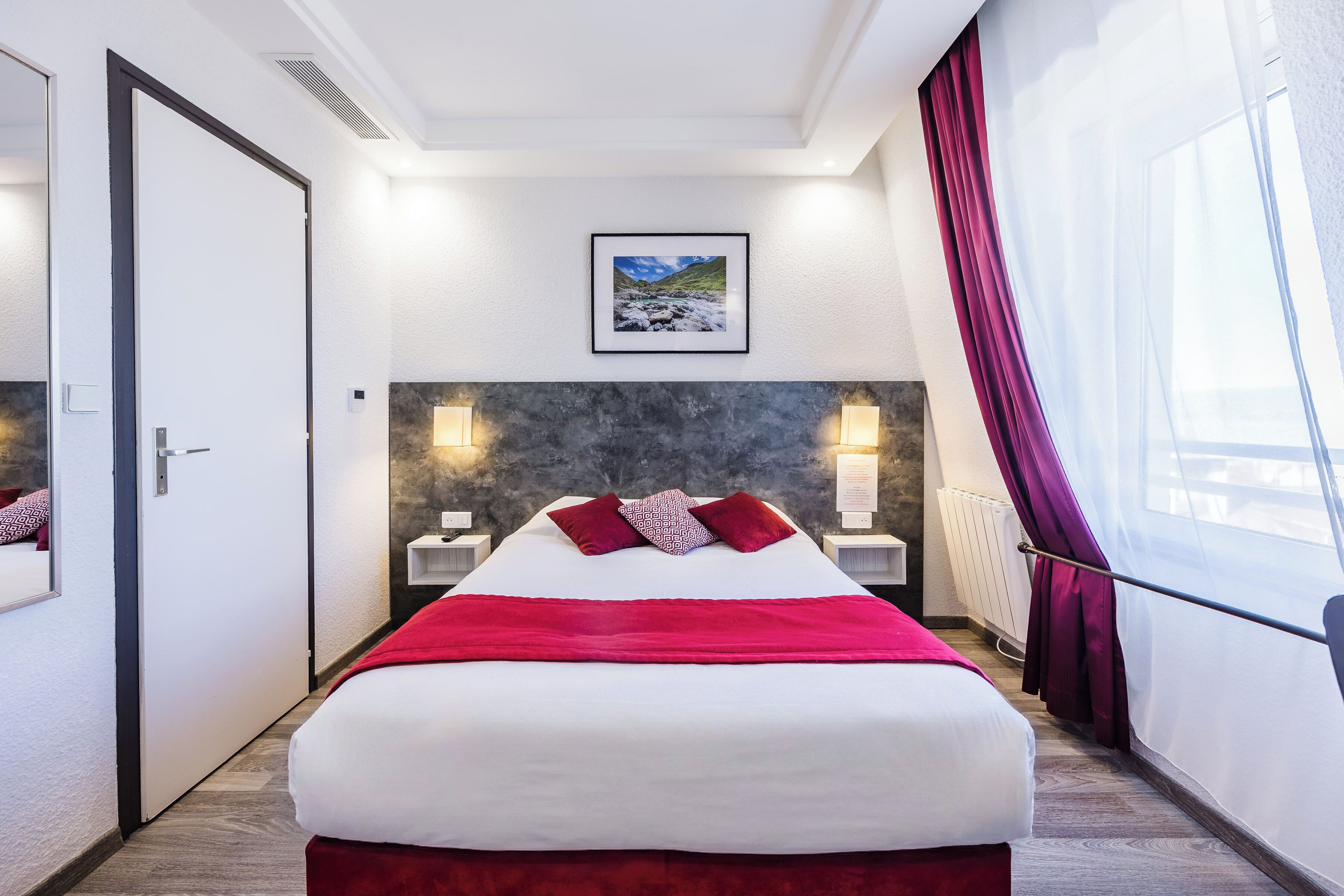 Een hotelkamer met een groot bed, een lijst met een afbeelding aan de muur en een raam met gordijnen.