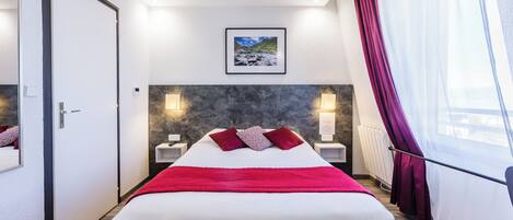 Een hotelkamer met een groot bed, een lijst met een afbeelding aan de muur en een raam met gordijnen.