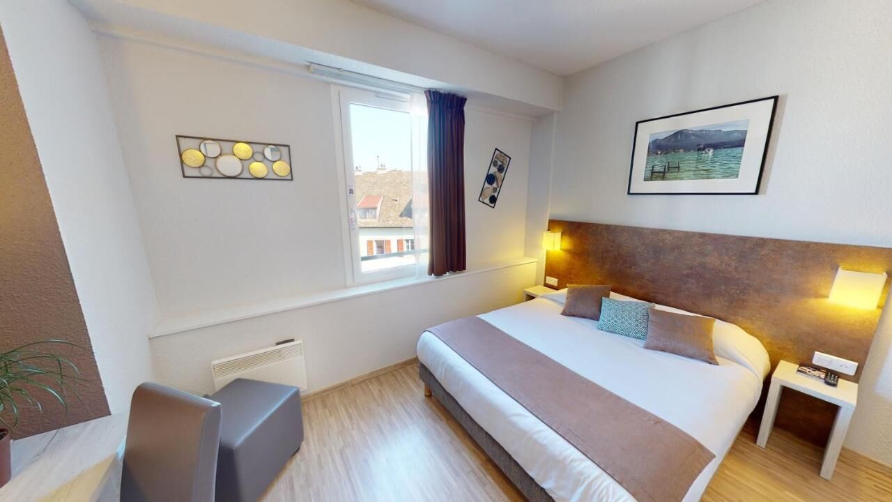 A modern hotel room with a large bed, bedside tables, a desk, and a window with curtains.