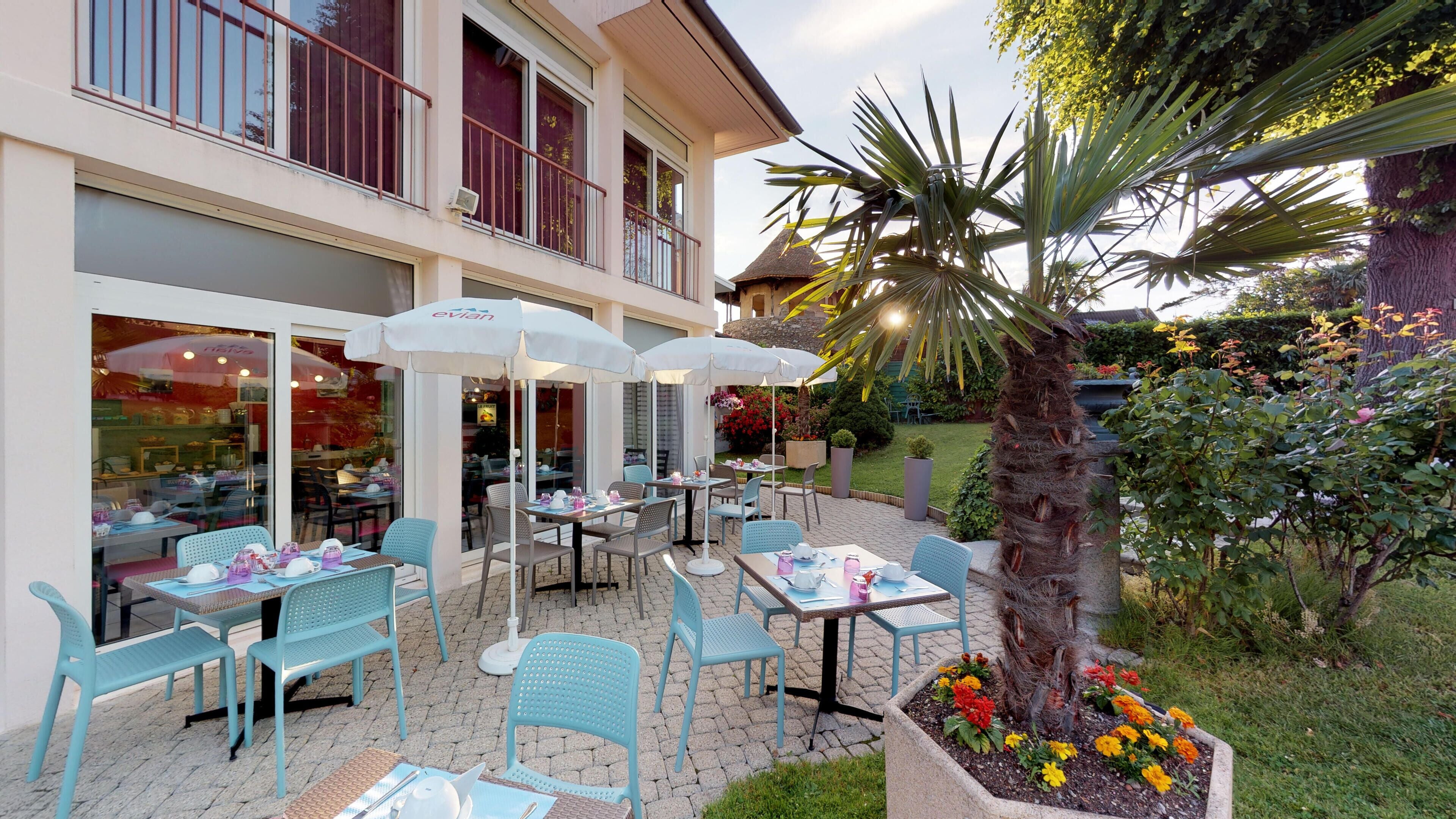 An outdoor seating area with tables and chairs, a palm tree, and a flower bed.