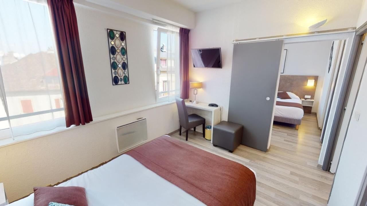 Ein Hotelzimmer mit Bett, Schreibtisch, Stuhl und Blick auf ein weiteres Zimmer.