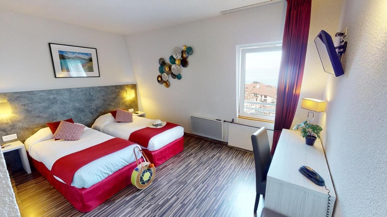 Ein Hotelzimmer mit zwei Betten, einem Schreibtisch, einem Stuhl, einem Fenster mit Aussicht und einer Wandlampe.