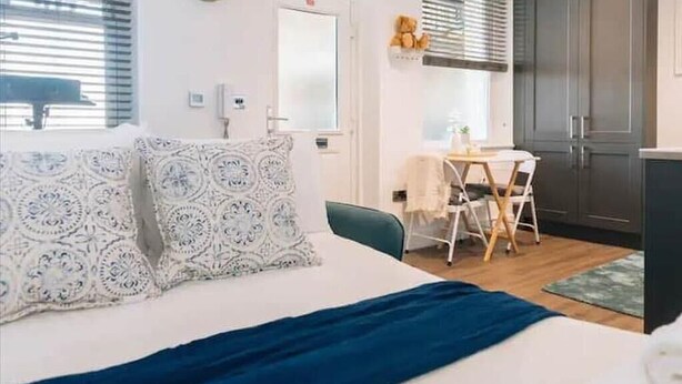 A bedroom with a bed, a bedside table, a chair, and a small desk with a chair. - Designer Flat in Heart of Brighton - Walk to Beach & Attractions! (Brighton and Hove)