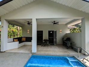 A covered outdoor area with a pool, seating, ceiling fans, and a grill.