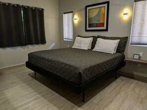 A bedroom with a bed, two bedside tables, a wall-mounted light, and a window with blinds.