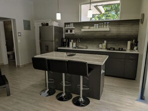 A modern kitchen with a central island, bar stools, and a view of the outdoors.