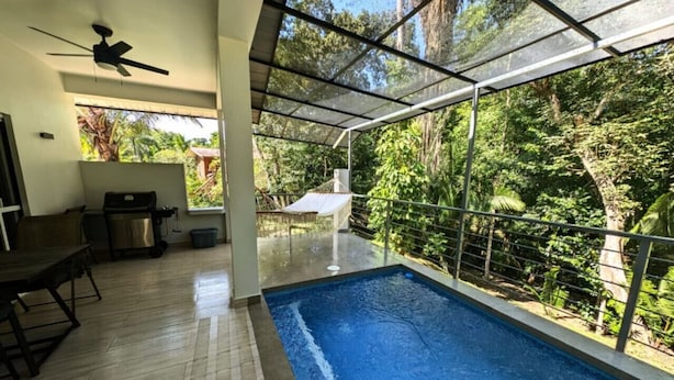 Ein überdachter Innenpool mit Glasdach, Deckenventilator und Blick auf die umliegende Grünfläche.