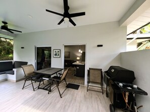 A modern outdoor living area with a dining table, chairs, a grill, and a ceiling fan.