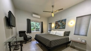 Ein Schlafzimmer mit Bett, Schreibtisch, Stuhl, Deckenventilator und einem Fenster mit Vorhängen.