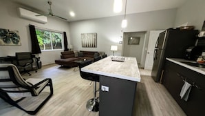 Eine moderne Küche mit einer zentralen Kochinsel, einem Essbereich mit einer Couch und einem Arbeitsplatz mit Stuhl und Schreibtisch.