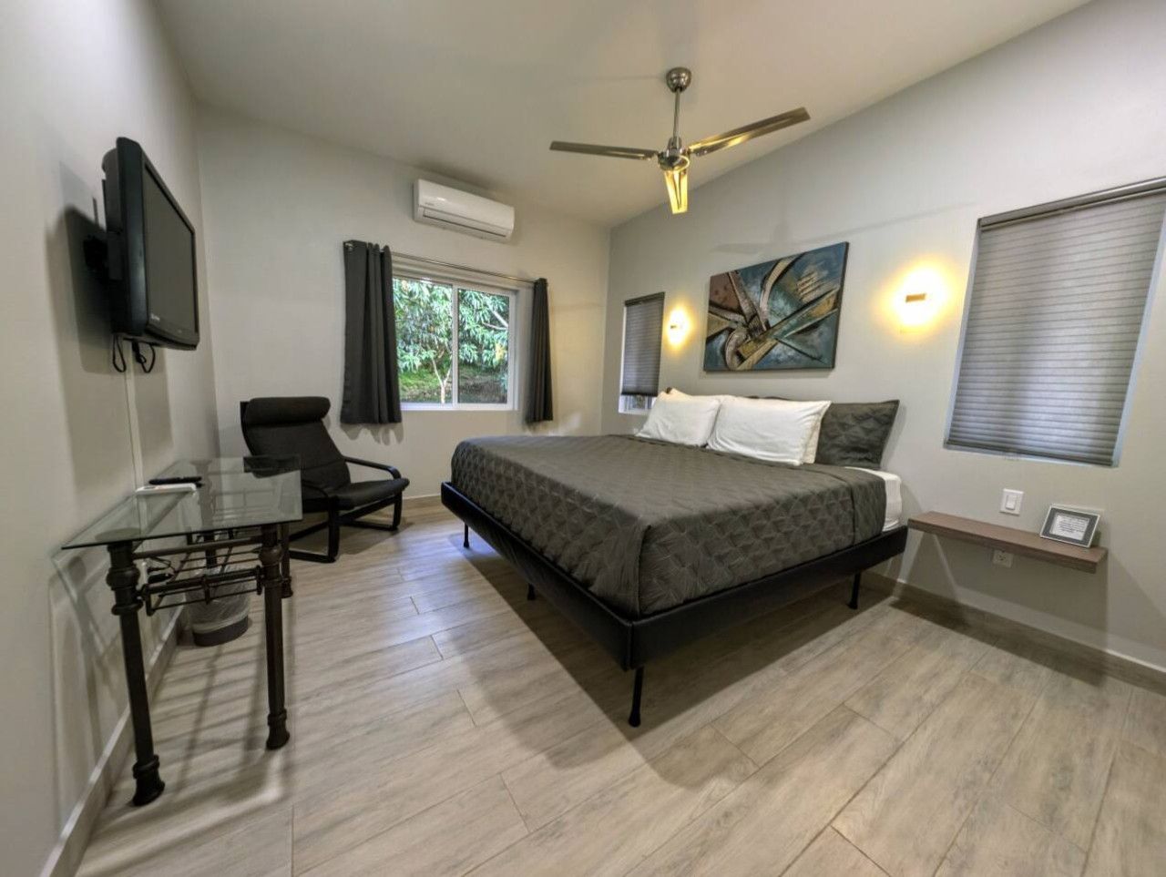 A bedroom with a bed, a desk, a chair, a ceiling fan, and a window with curtains.