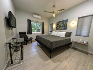 A bedroom with a bed, a desk, a chair, a ceiling fan, and a window with curtains.