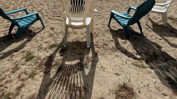 A beach with three chairs and a bench, a calm lake, and a cloudy sky. - RUSTIC LAKESIDE COTTAGE. LARGE SANDY BEACH (Sebago)