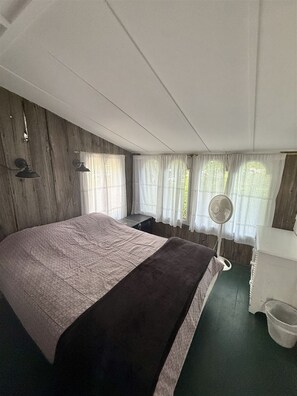 Une chambre à coucher avec un lit, une table de chevet, un ventilateur et une fenêtre avec des rideaux.