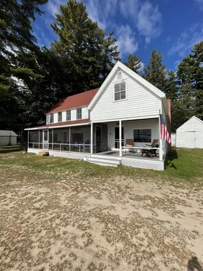 Een wit huis met twee verdiepingen, een rood dak, een veranda met zitplaatsen buiten en een Amerikaanse vlag.