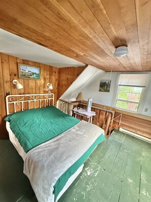 Een kamer met een bed, houten wanden, een raam en een schilderij aan de muur.