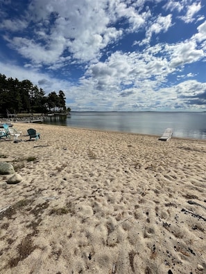 A beach with a sandy shore, a few lounge chairs, and a calm body of water. - LARGE RUSTIC COTTAGE. SEBAGO LAKE BEACHFRONT (SEBAGO)