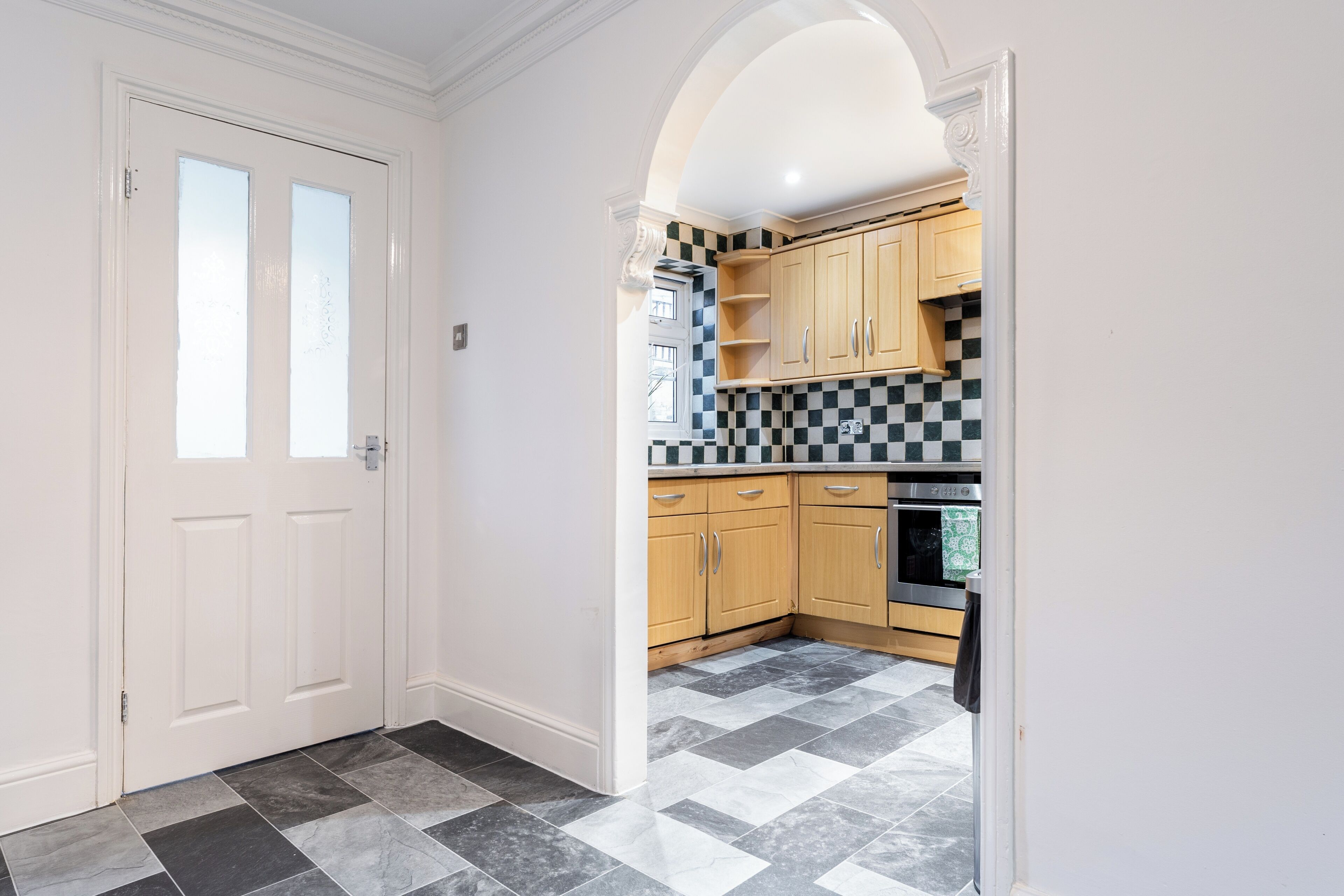 A kitchen with checkered tiles, wooden cabinets, and a modern oven.