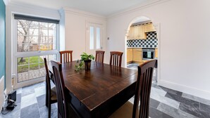 Comedor con una mesa y sillas de madera oscura, una planta en maceta y vistas a la cocina a través de un arco.