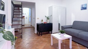 A living room with a grey sofa, a white coffee table, a black side table, and a white wardrobe. There is a staircase leading to another room.