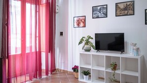 A living room with a TV on a white stand, red curtains, and three framed pictures on the wall.