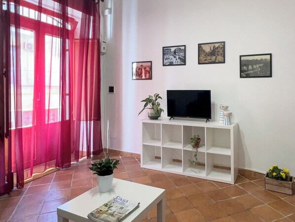 Una sala de estar con un televisor sobre un mueble blanco, una revista sobre una mesa y tres cuadros en la pared.