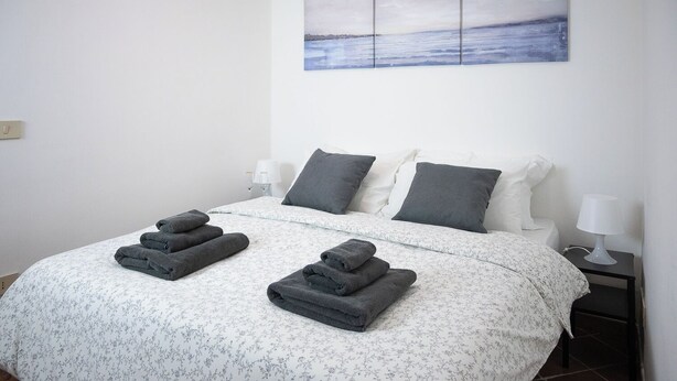 A neatly made bed with a floral-patterned bedspread, two pillows, and two folded towels on the bed.