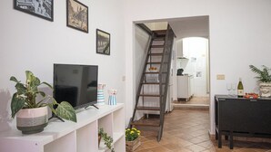 A living room with a TV, a plant, and a ladder leading to a kitchen.