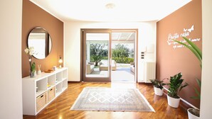 Ein modernes Interieur mit Holzboden, einem weißen Konsolentisch, einem Spiegel und Blick durch eine Glastür auf einen Außenbereich mit Sitzgelegenheiten.