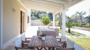 An outdoor patio with a wooden table and chairs, a wicker sofa, and a potted plant. - Villa Don Sante In Locorotondo (Fasano)