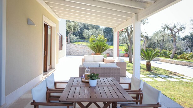 Eine Terrasse im Freien mit einem Holztisch und -stühlen, einem Rattansofa und einem Blumentopf.