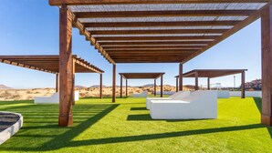 An outdoor seating area with white sofas under wooden pergolas, surrounded by artificial green grass, with a desert landscape in the background. - Villa Majanicho with pool (Majanicho)