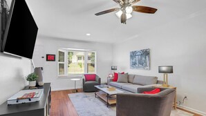 A modern living room with a grey sofa, a coffee table, and a TV mounted on the wall. - 0.5 mi UGA Stadium & Campus– 2 BR 2.5 BA Athens Townhome with King, Queen + Twin (Athens)