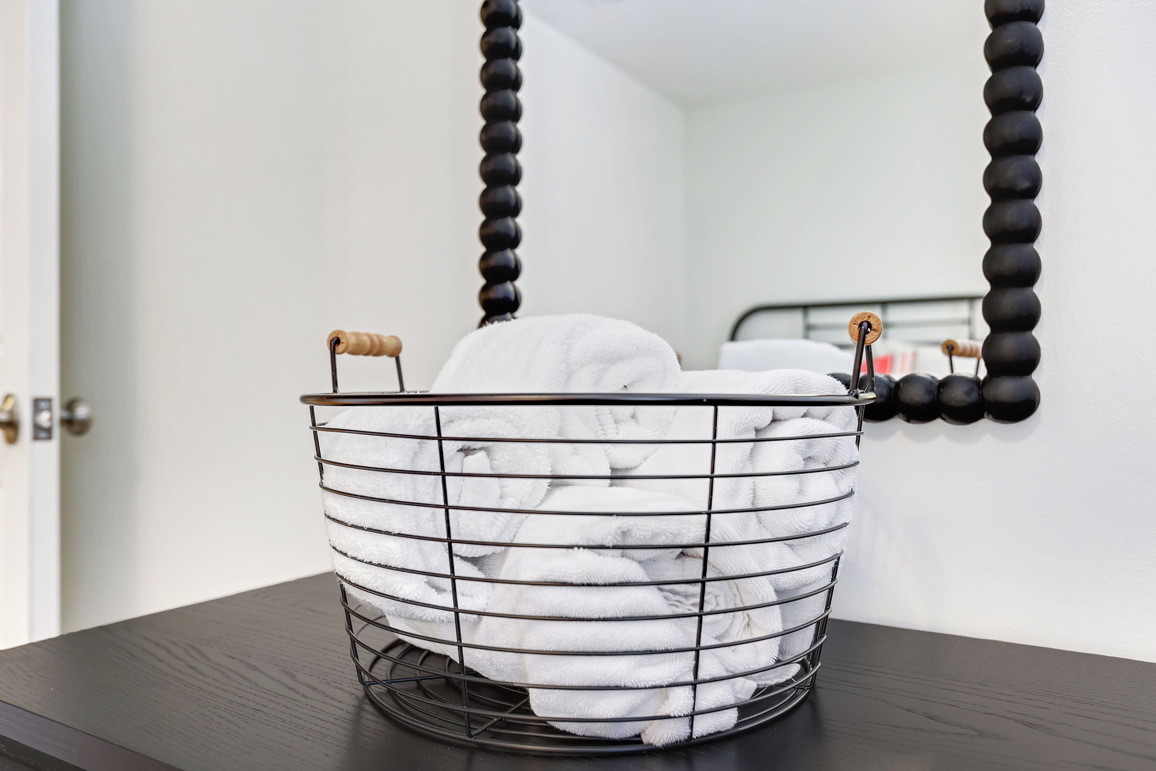 A metal basket filled with white towels on a dark wooden table.
