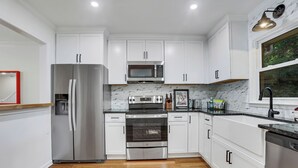 A modern kitchen with white cabinets, stainless steel appliances, and a wooden floor. - 0.5 mi UGA Stadium & Campus– 2 BR 2.5 BA Athens Townhome with King, Queen + Twin (Athens)