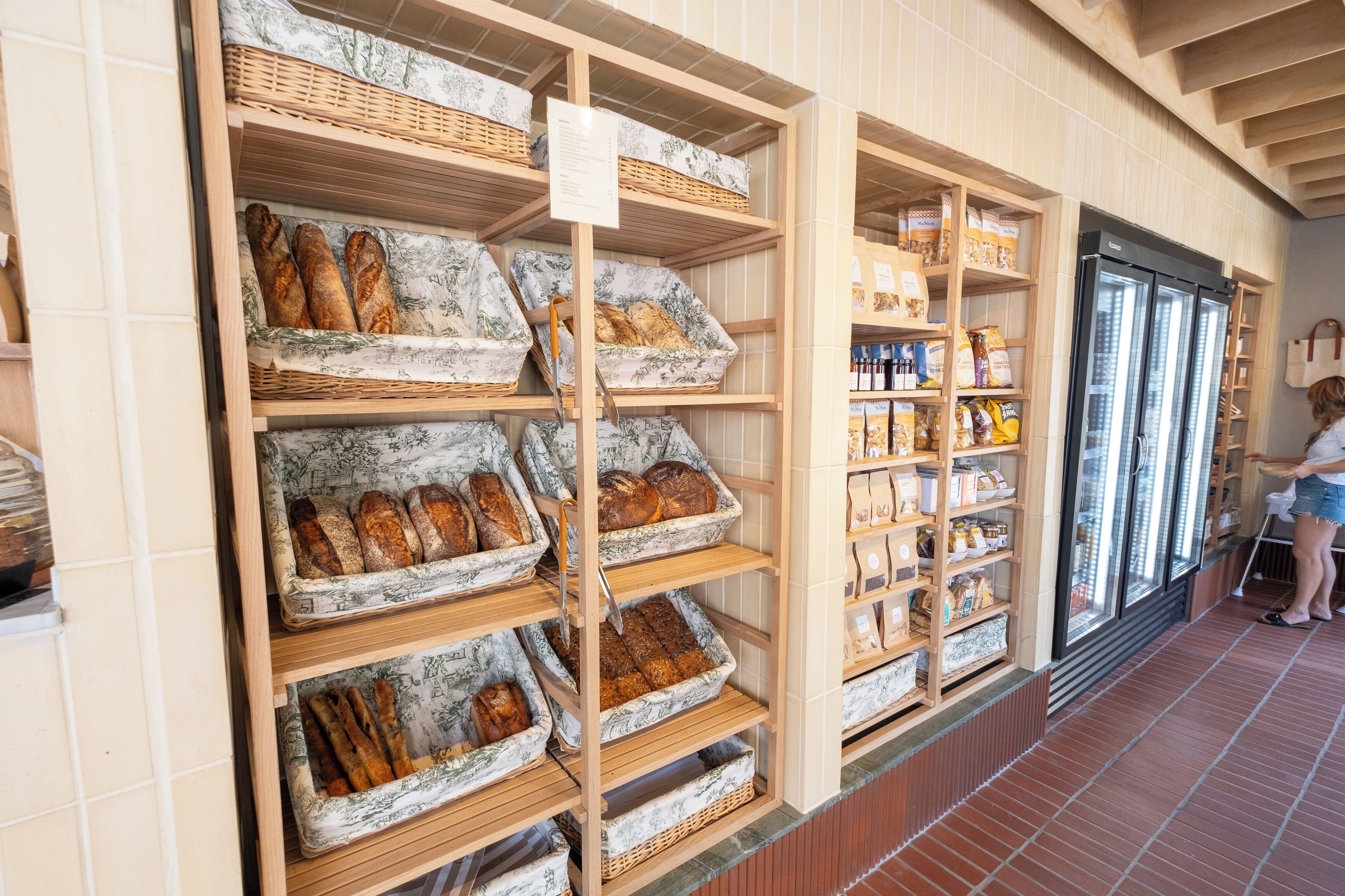 A bakery display with bread and pastries in wicker baskets, a refrigerated display case, and a tiled floor.