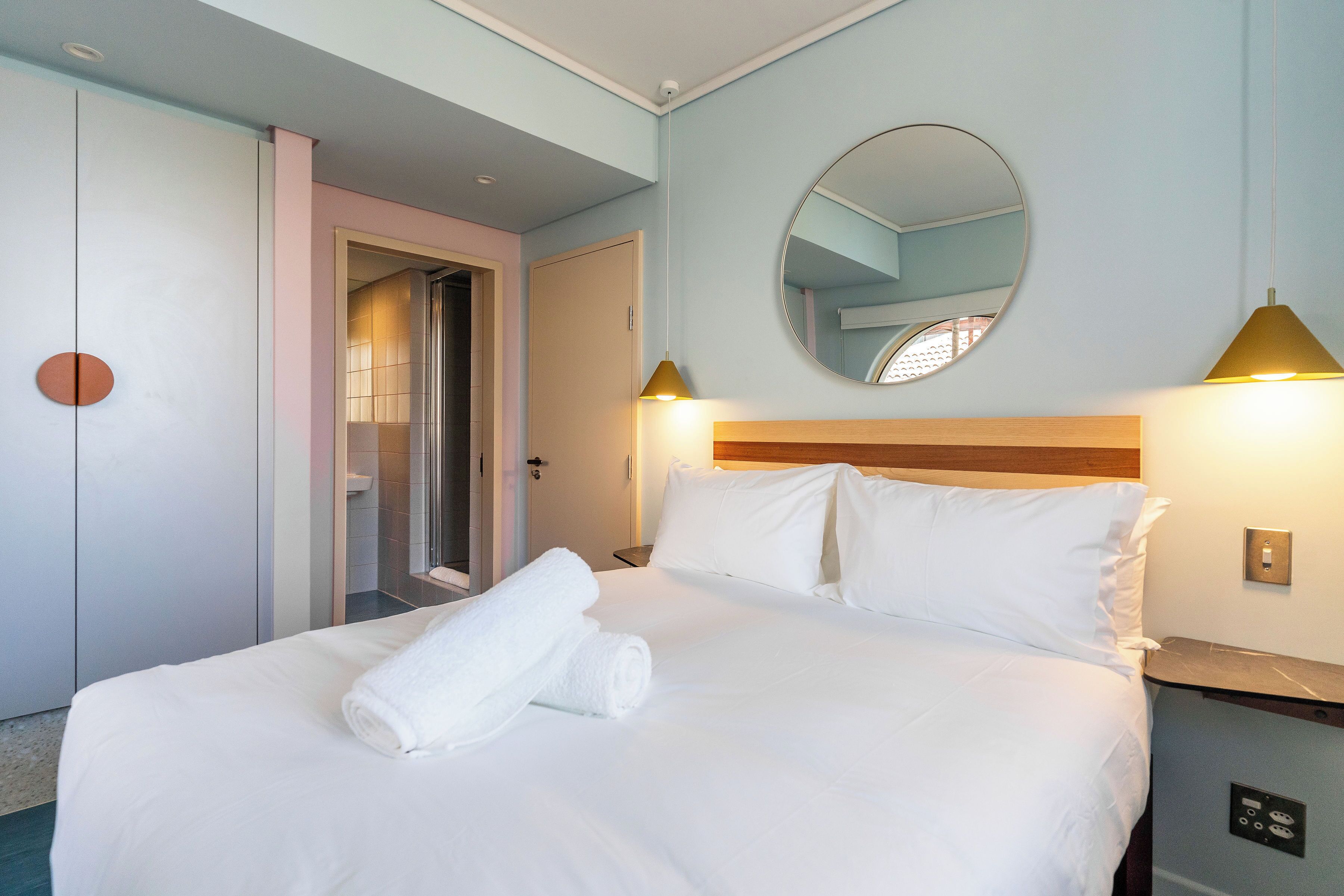 Quarto de hotel com cama, espelho e mesa de cabeceira.