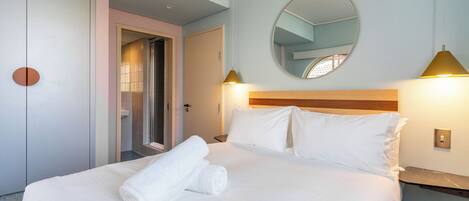 Quarto de hotel com cama, espelho e mesa de cabeceira.